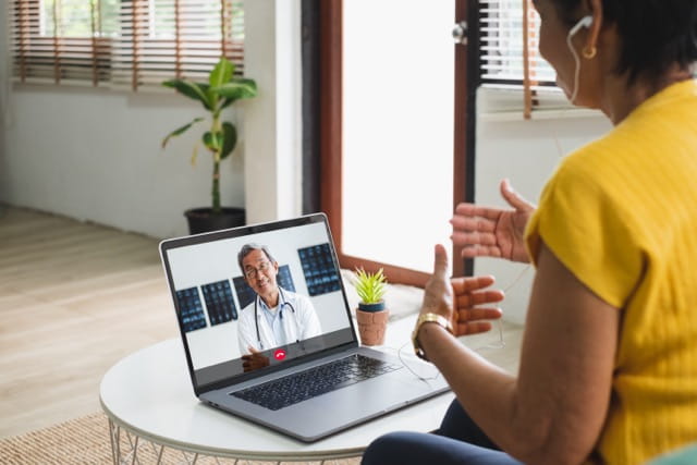 A woman uses a laptop to video chat with a provider