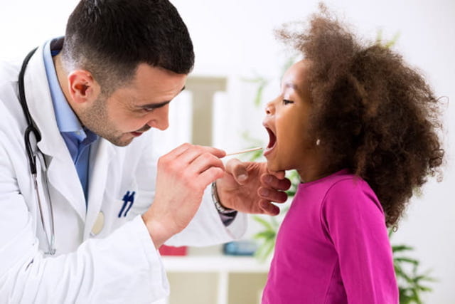 A provider uses a tongue depressor to look inside a child's mouth