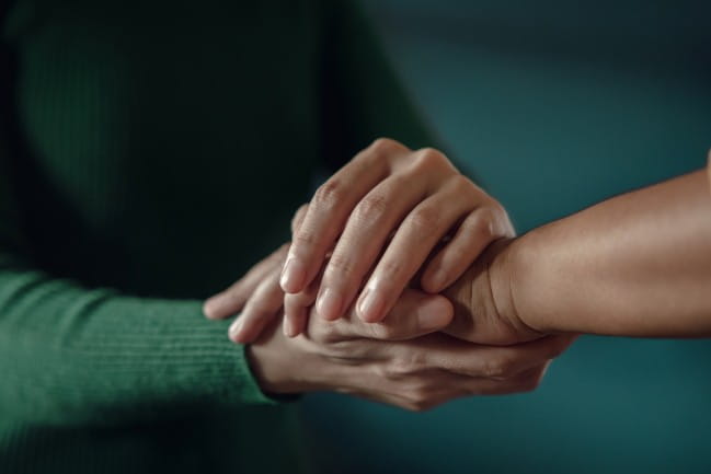 Closeup of people holding hands in a supportive way.
