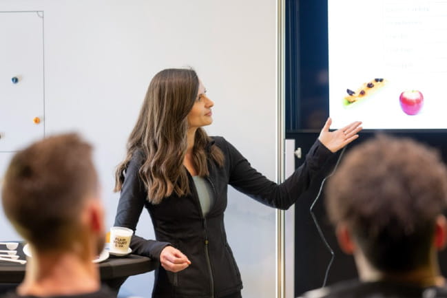 A woman pointing to an apple on the screen of a presentation she is giving.