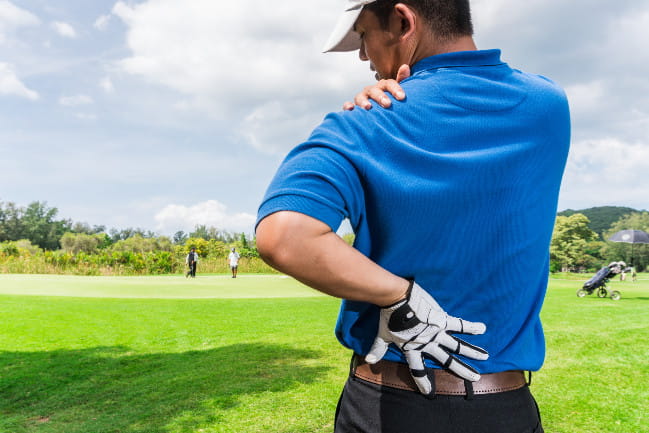 A person that has been out golfing is holds touches their shoulder and their back in pain.