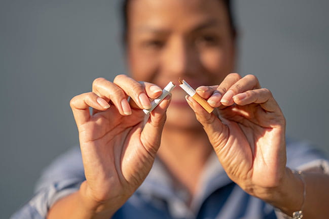 A smiling woman breaking a cigarette in half.