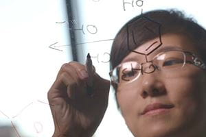 Image of scientist using a clear board to diagram molecules