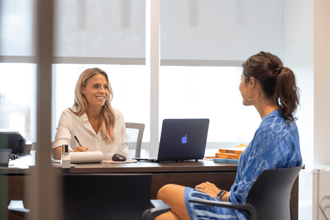 woman behind desk smiling at another woman while writing notes MUSC health coach certification