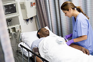 Photo of a nurse preparing an intravenous line for a patient lying in a patient bed.