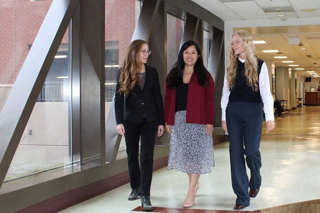 Three women walking down a long corridor.