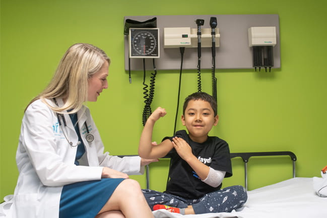 Dr. Hudspeth next to a pediatric patient flexing his bicep in front of a green wall.