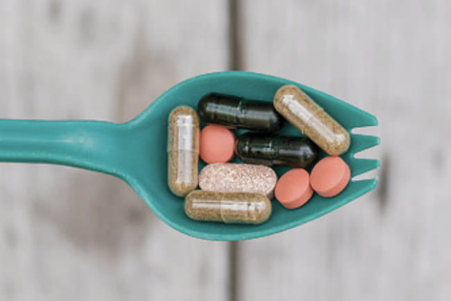 Image of a green spork that is holding a variety of pills.
