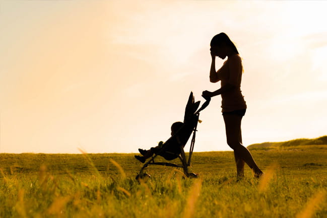 new mom pushes her baby in a stroller in a field at sunrise