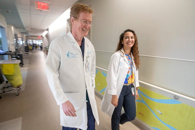 two doctors in white coats walk and talk in a hallway