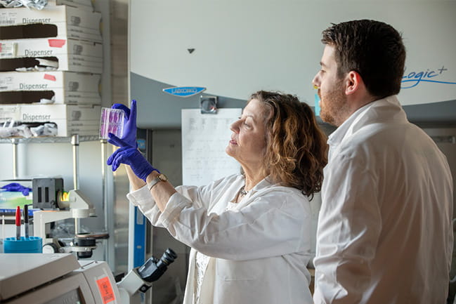 Paula Traktman, Ph.D. and Conor Templeton, Ph.D. in white coats in the lab examine cells in the lab.