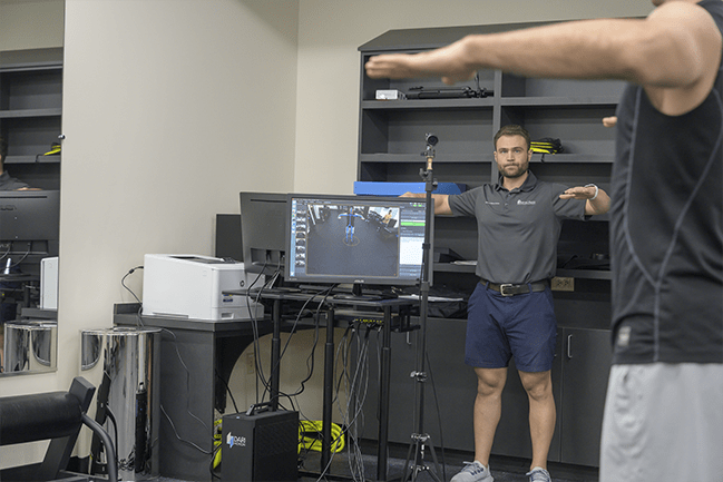 Technician demonstrating arm movement for client, with motion capture platform showing real-time data