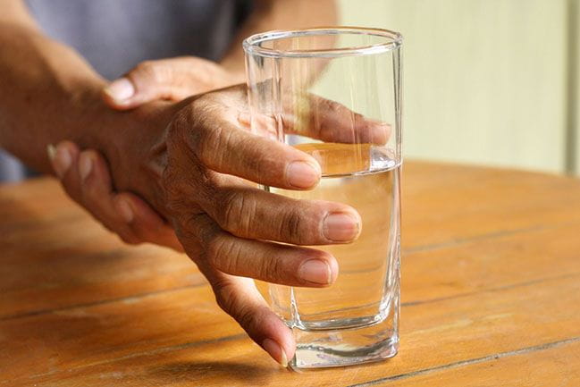 Elderly person’s hand holding glass of water with support from other hand