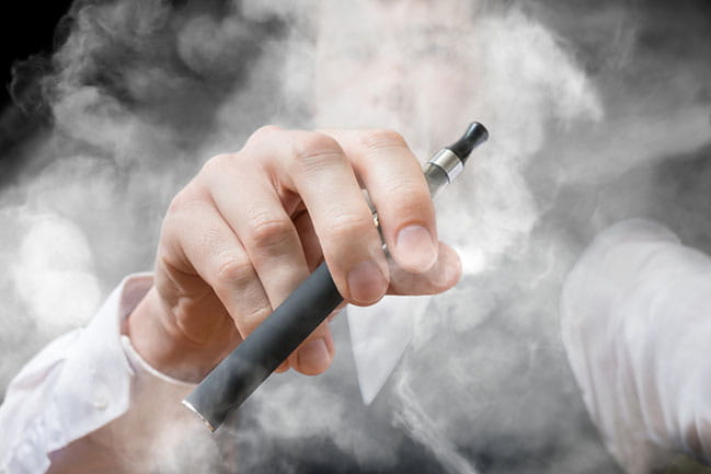 Man’s hand holding e-cigarette surrounded by vapor.