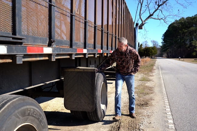 A man by the side of a road inspecting the trailer of an 18-wheeler.