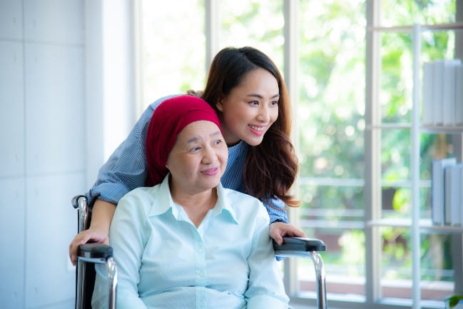 Smiling woman leaning in behind another woman in a wheelchair.