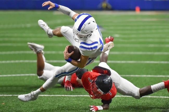 Two (American) football players. One is trying to tackle the other. Player with the ball is in mid-air.