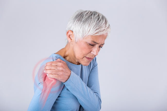 Woman holding her right shoulder with an illustration of upper arm and shoulder bones superimposed.