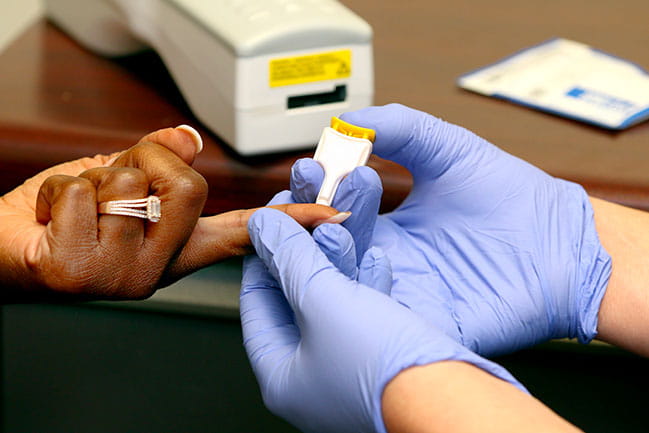 care team member performing finger prick on patient