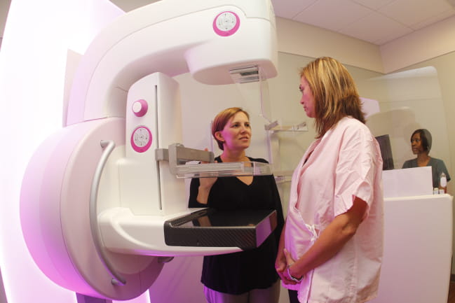 Radiology technician talking to patient in front of the mammography machine.