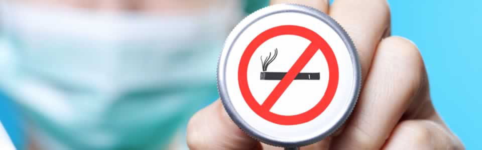 Person holding a button that shows a red line crossing through a smoking cigarette.