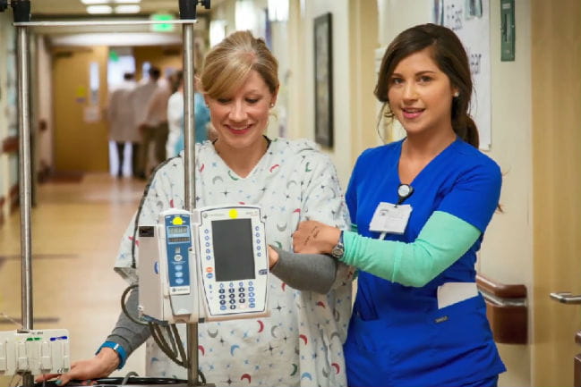 Care giver assisting Kidney Transplant patient walk down hospital hallway.