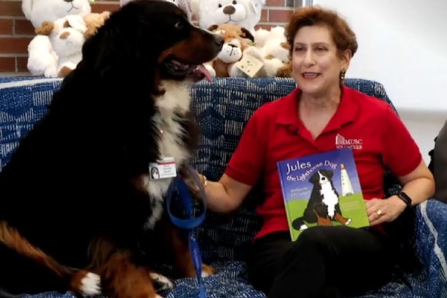 Liz reading a book with MUSC pet therapy dog, Martel.