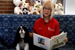 Marsha reading a book with MUSC pet therapy dog, Rose.