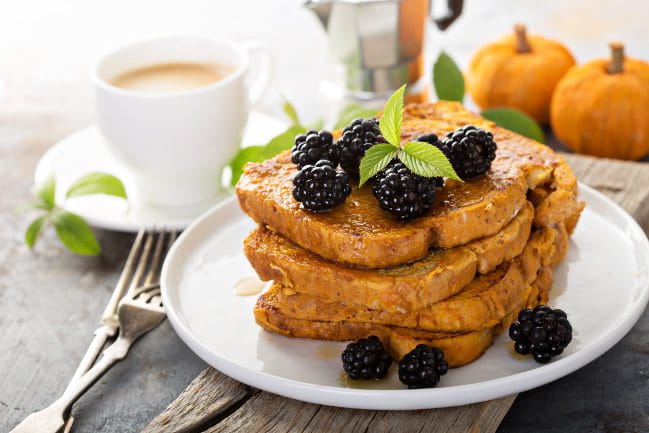 An image of french toast stacked on a white plate topped with blackberries.