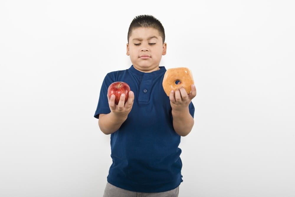 Child holding an apple in one hand and a doughnut in another.