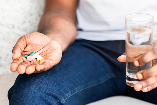 A sitting figure holding vitamins in one hand and a glass of water in the other. 