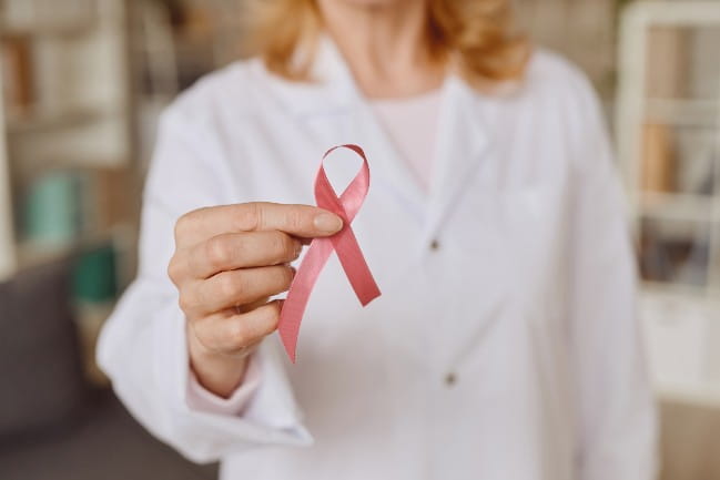 A doctor holding a pink ribbon for breast cancer awareness.