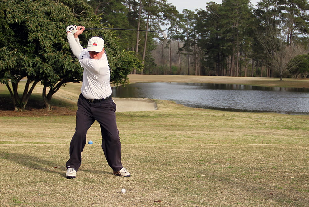 A man takes a swing at a golf ball on a golf course 