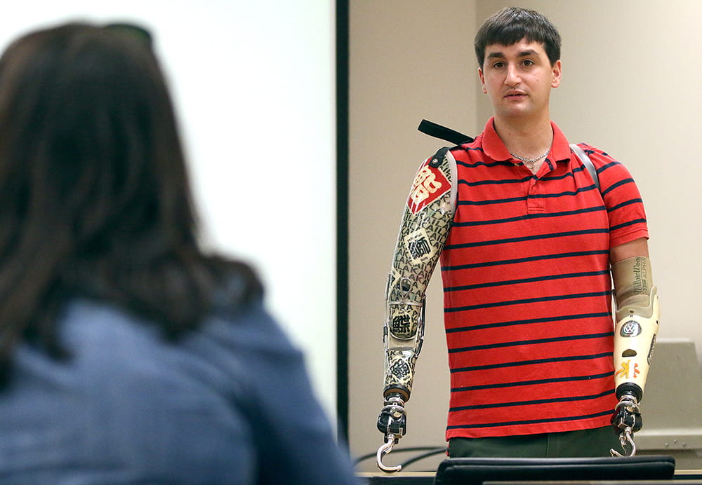 A man with two prosthetics for arms speaks in a classroom 