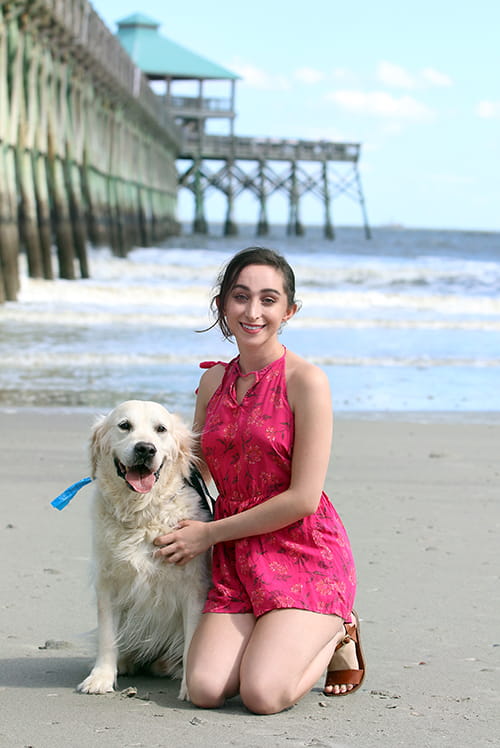 a young woman in a bright pink outfit poses on the beach next to her dog 