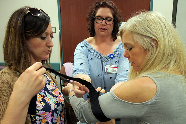 School nurse Julie McElroy, who works at Chicora Elementary, learns how to use a tourniquet on fellow nurse Marjorie Bailey, who works at Moultrie Middle School. MUSC clinical instructor Sarah Gay, middle, shows them how it works.
