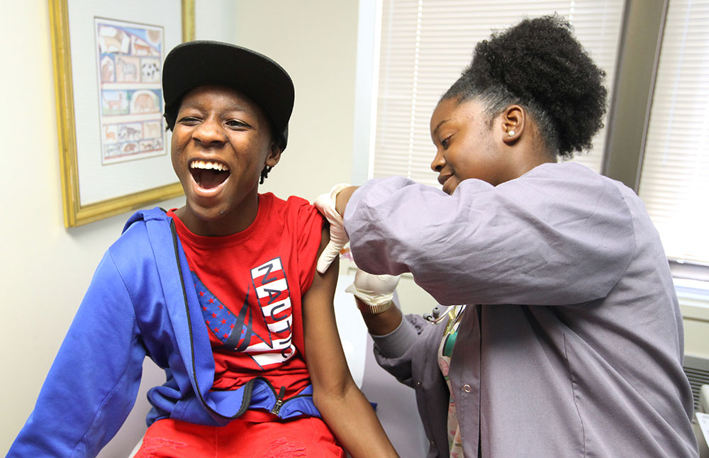 Braxton Fludd hams it up for the camera while getting a shot from certified medical assistant Shavazae Rivers. Photo by Sarah Pack