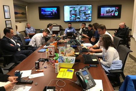 A look inside the command center at MUSC. Monitors on walls show locations across campus as people work on computers around a conference table