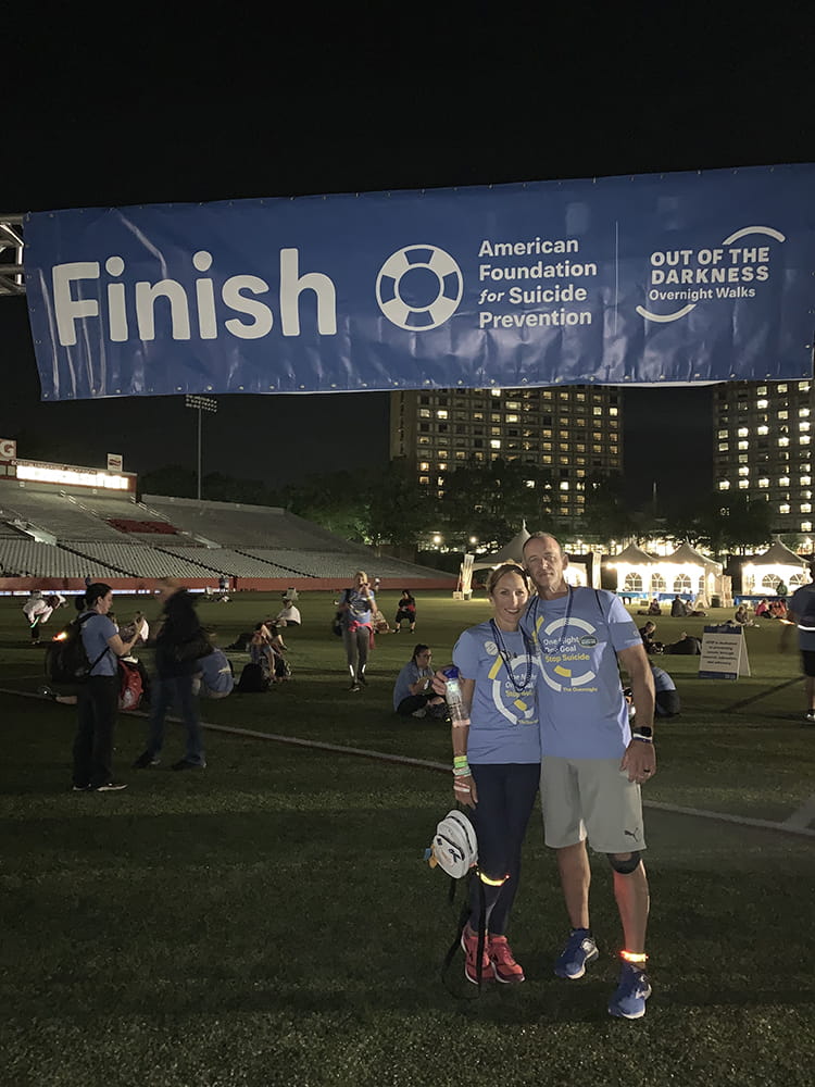 A man and woman at a large finish sign in the dark