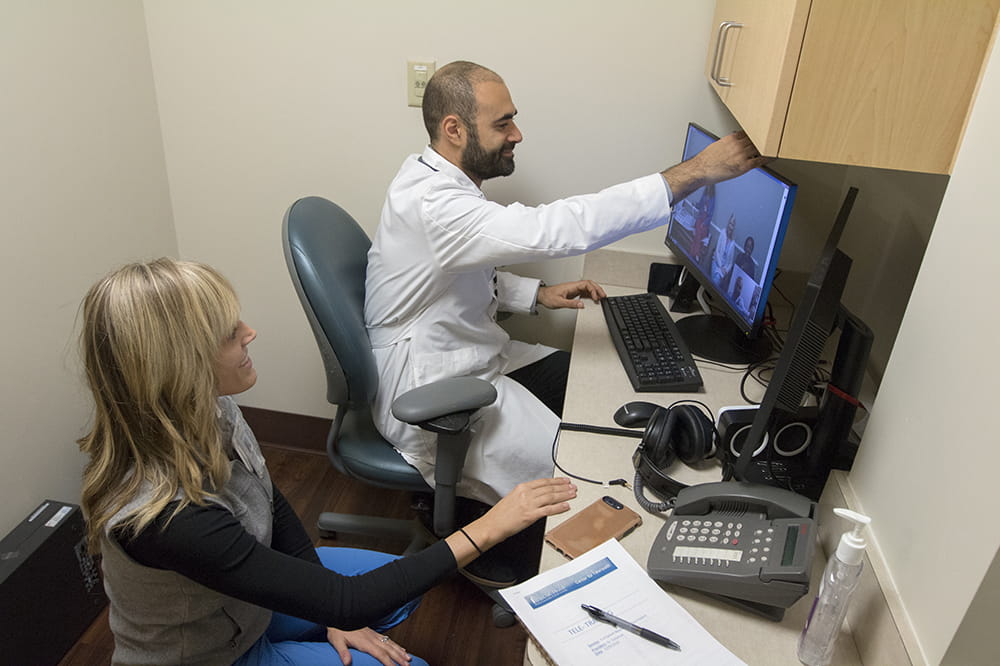 Dr. Soliman adjusts the camera on his computer screen in a small closet-like room as he prepares for telehealth visits. 