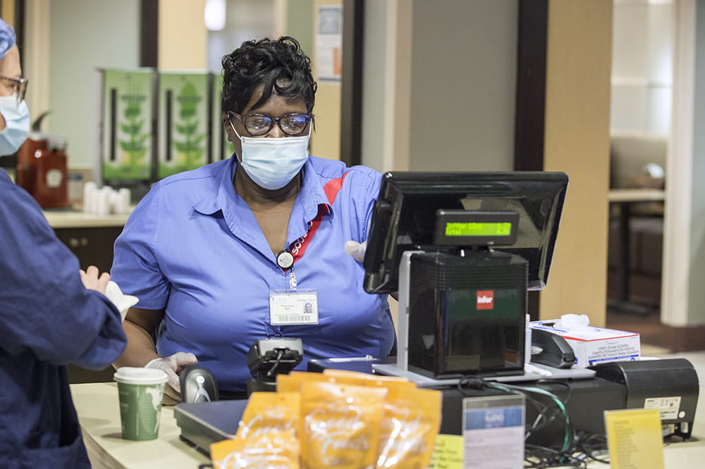 A woman in a mask rings up another woman in a mask in the hospital cafeteria