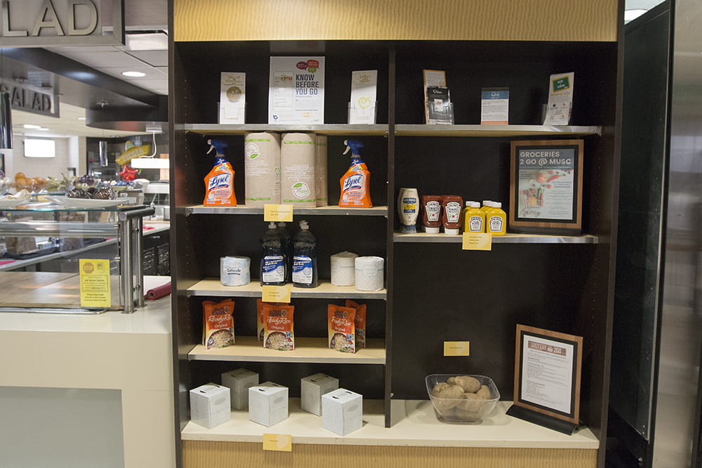 a photo of shelves in the cafeteria with various items like Lysol spray, toilet paper, ketchup, mustard and potatoes. 