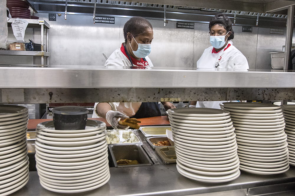 Two cooks are visible behind stacks of plates