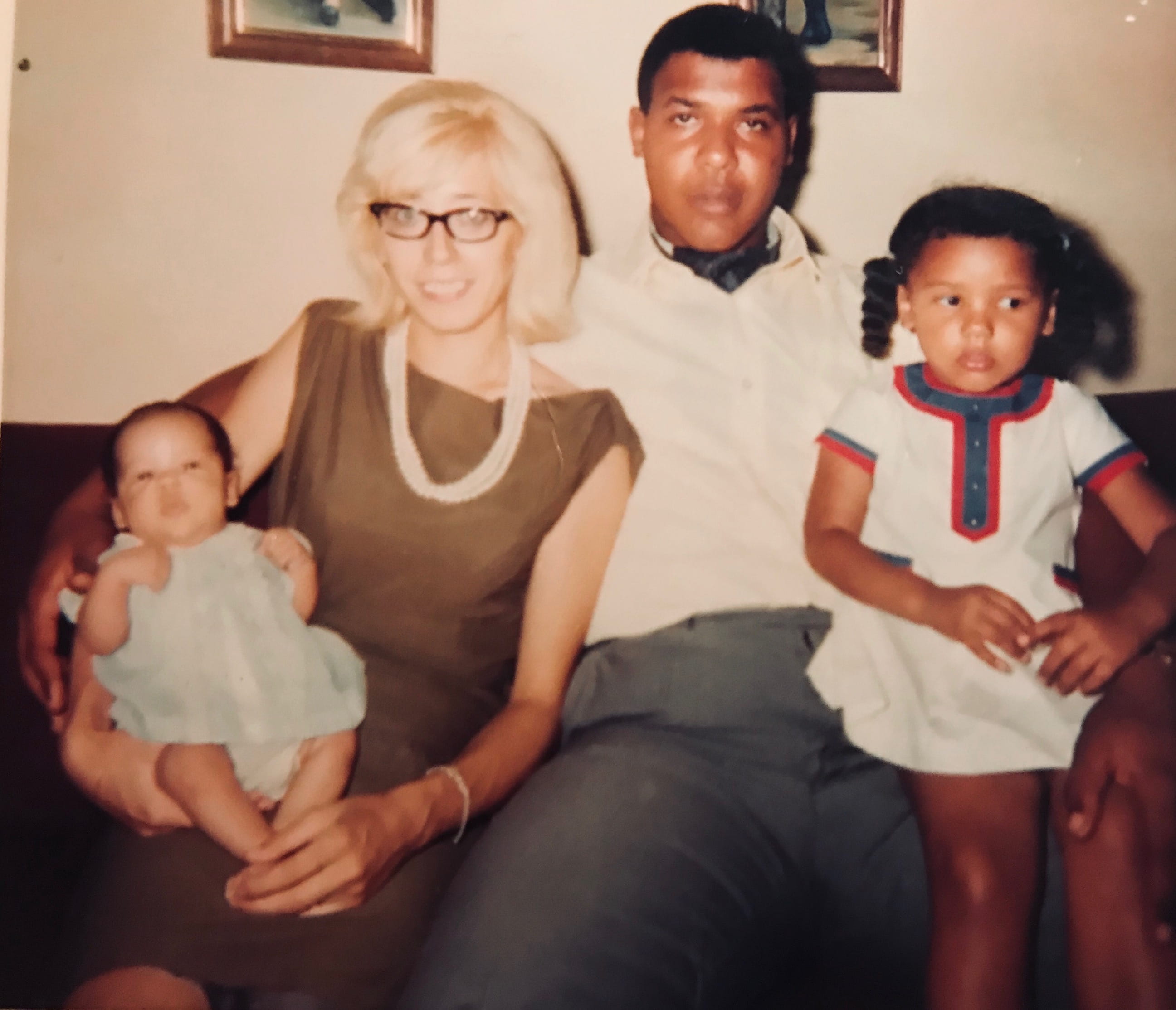 old photo of family sitting on couch. there is a mom and dad and on either end is a baby and an toddler