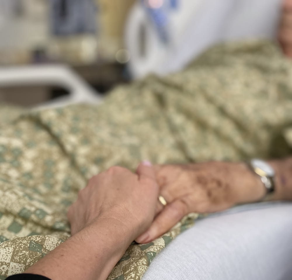 Two people, one in a hospital bed, holding hands