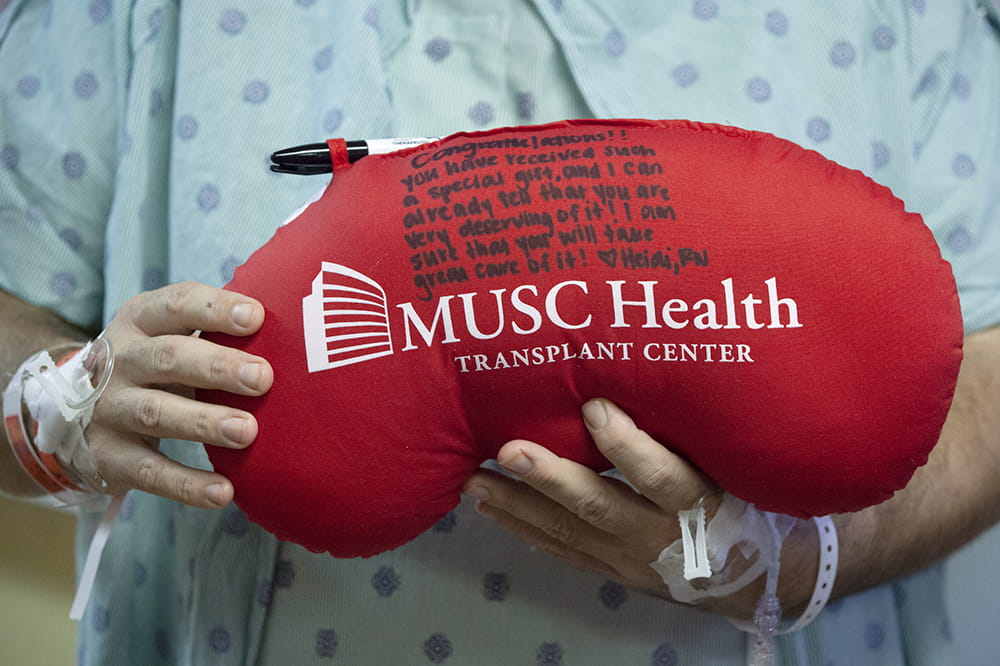 Red kidney shaped pillow with an encouraging note written on it from a nurse to Thomas Banks.