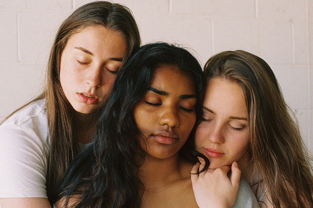 Three young women hugging with their eyes closed.