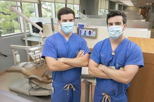 twins in blue scrubs and face masks pose within a dental clinic