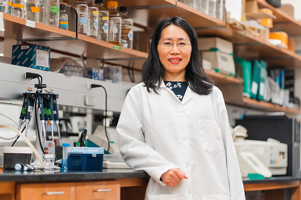 Dr. Jen Wang stands in front of shelves of equipment in her lab