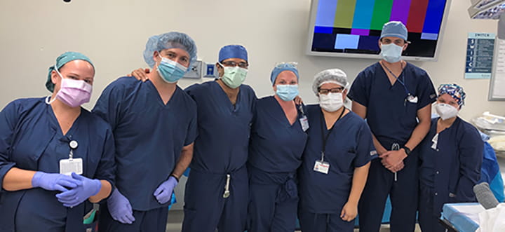 a group of people in dark blue scrubs and operating room caps pose